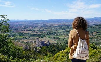 A imagem mostra uma participante do projeto Economia de Francisco na frente de uma paisagem com muita natureza para sugerir a presença da iniciativa no mundo