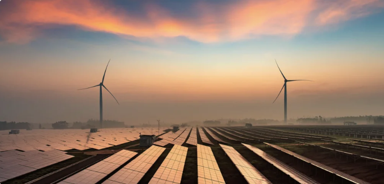Vemos um campo de produção de energia limpa, com hélices e placas solares. Ao fundo, um entardecer